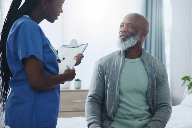 Healthcare professional speaking with an older adult patient during a clinical visit, discussing health and wellness in a medical exam room.