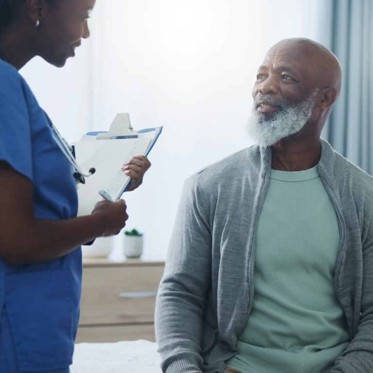 Healthcare professional speaking with an older adult patient during a clinical visit, discussing health and wellness in a medical exam room.