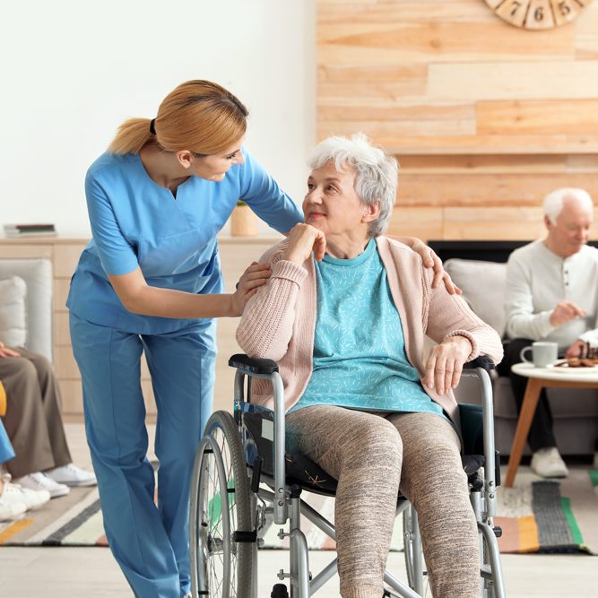 Nurse assisting an older woman in a wheelchair at a residential care facility.