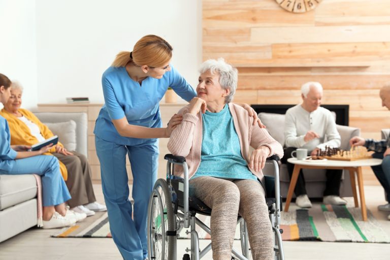 Nurse assisting an older woman in a wheelchair at a residential care facility.